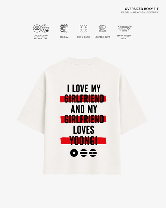 A white oversized boxy-fit T-shirt shown from the back, featuring a humorous printed slogan in black text with red highlight bars and black emoji faces. The image includes feature icons and text at the top detailing the fabric's properties.