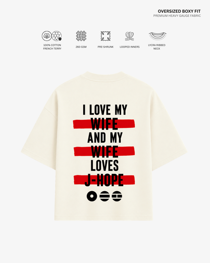 An oversized cream-colored T-shirt shown from the back, featuring a bold graphic print with black text and red horizontal stripes. The text reads 'I LOVE MY WIFE AND MY WIFE LOVES J-HOPE'.