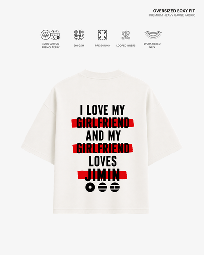 An oversized white boxy-fit t-shirt with a humorous graphic on the back. The graphic features the text 'I LOVE MY GIRLFRIEND AND MY GIRLFRIEND LOVES JIMIN' printed in black, with each word 'GIRLFRIEND' highlighted by a red brushstroke background.